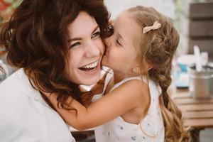 retrato de una pequeña hija besando a su hermosa y feliz madre foto