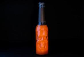 Orange Halloween cocktail in a glass bottle with a skull on a black background. Space for text photo