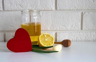 un corazón de madera roja y remedios naturales para el resfriado sobre una mesa blanca sobre un fondo de ladrillo. ajo, miel, limón, aloe remedios caseros para los resfriados de otoño, covid 19 foto