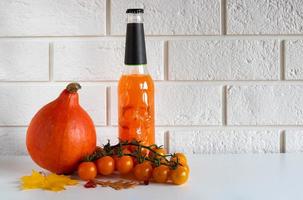 A bottle of orange drink with a skull, ripe pumpkin vegetables and orange cherry tomatoes on a white background.Halloween concept. Place for your text photo