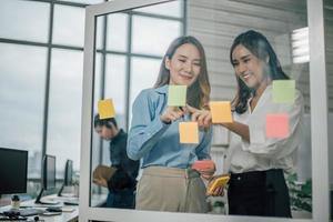 Asian two woman smiling and using post it notes to share about project. photo