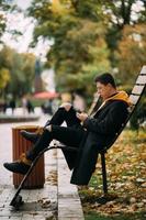 joven sentado en un banco en el parque y escuchando música foto