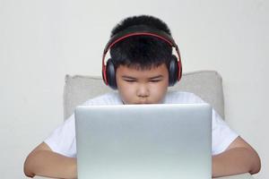 The boy sit on sofa is using laptop and wearing headphones. Education, learning and technology concept. photo