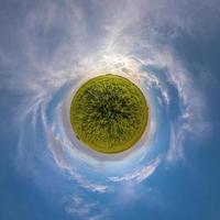 green tiny planet in blue sky with beautiful clouds. Transformation of spherical panorama 360 degrees. Spherical abstract aerial view. Curvature of space. photo