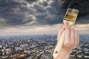 paintbrush paints storm clouds over dark city photo