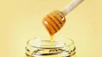 Honey dripping from a honey dipper into a glass honey jar with plain background. video
