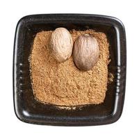 whole nutmeg seeds and powder in black bowl photo