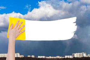 hand deletes rainy clouds over city by yellow rag photo