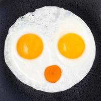 fried eggs and slice of carrot on plate close up photo