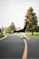 atleta mujer saltando salto mortal en la carretera, haciendo ejercicios al aire libre. foto