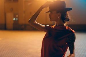 The young, attractive girl in a hat poses to the camera at night photo