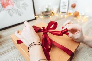Woman wrapping present in paper with red ribbon. photo