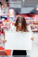 Smiling brunette woman holding white blank board photo