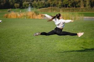 la chica deportiva saltando en el aire sobre la naturaleza demuestra un estiramiento perfecto. foto