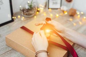 Woman wrapping present in paper with red ribbon. photo