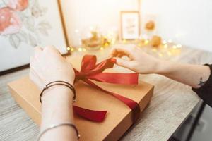 Woman wrapping present in paper with red ribbon. photo