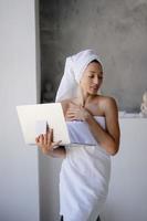 Woman freelancer in white towel stand in the bathroom with a laptop photo