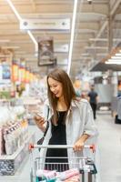 Smiling young woman with smartphone in supermarket photo