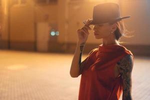 The young, attractive girl in a hat poses to the camera at night photo