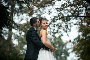 groom embracing bride from back photo