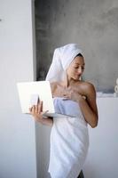 Woman freelancer in white towel stand in the bathroom with a laptop photo