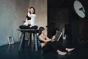 two girls are posing for the camera, one sitting on a table, other on the floor photo
