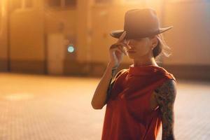 The young, attractive girl in a hat poses to the camera at night photo