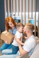 Young happy family with kid unpacking boxes together sitting on sofa photo