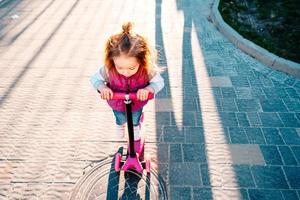 Little girl with blonde hair rides on scooter photo