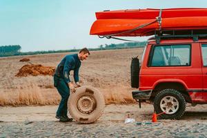 Man rolls a new replacement wheel to 4x4 off road truck photo