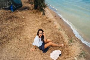 attractive woman in summer skirt and shirt sits on the shore photo