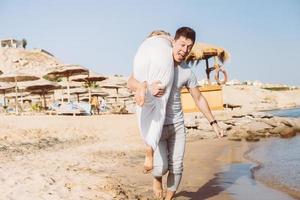 un chico cargando a una chica, en la playa foto