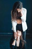 two girls are posing for the camera, one standing, other on the floor photo