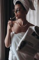 Beautiful young woman in a towel smokes a cigarette and reads newspaper photo