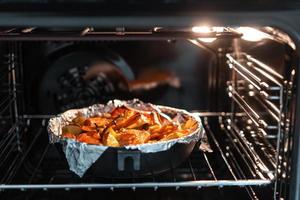 Baked potatoes with carrot and other spices in roasting pan. photo