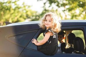 A little girl is sitting on the door of the car photo