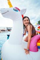Happy young woman sitting on inflatable unicorn toy mattress photo