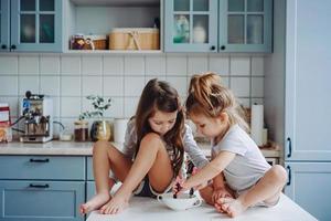 Two little girls in the kitchen sitting on the table. photo