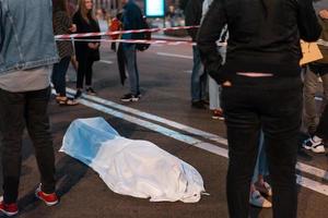 cuerpo humano cubierto por una sábana tirada en la calle. foto