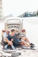 Couple sitting on the asphalt behind the car photo