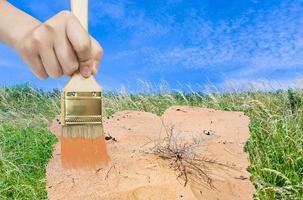 hand with paintbrush paints sand in green meadow photo