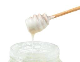 side view of white honey flows from stick into jar photo