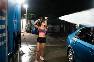 Young woman washing blue car at car wash photo