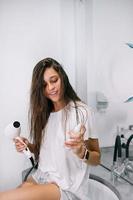 Young beautiful woman in the bathroom holding a hairdryer and a small bottle photo