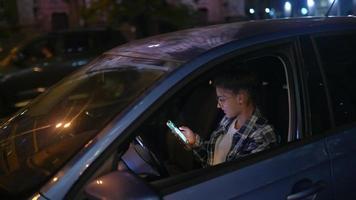 meisje zittend in geparkeerd auto gebruik makend van smartphone Bij nacht