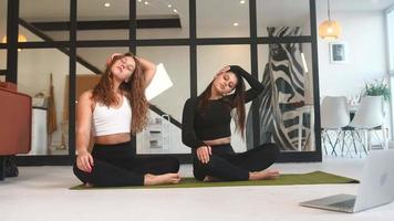 dos mujeres jóvenes hacen ejercicio en una alfombra de yoga en el suelo con una computadora portátil abierta cerca video