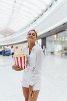 linda mujer joven sosteniendo palomitas de maíz en el fondo del centro comercial foto