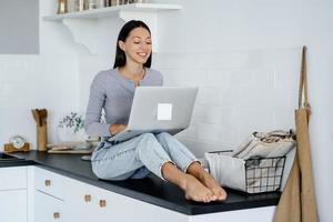 Image of cute brunette woman sitting at kitchen and using laptop photo