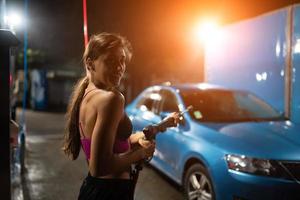 Young woman washing blue car at car wash photo