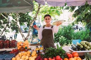 vendedora joven que sostiene el calabacín y el tomate en manos foto